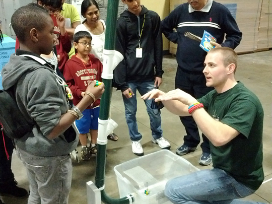 A tour guide explains the marble nuclei demo to a student.